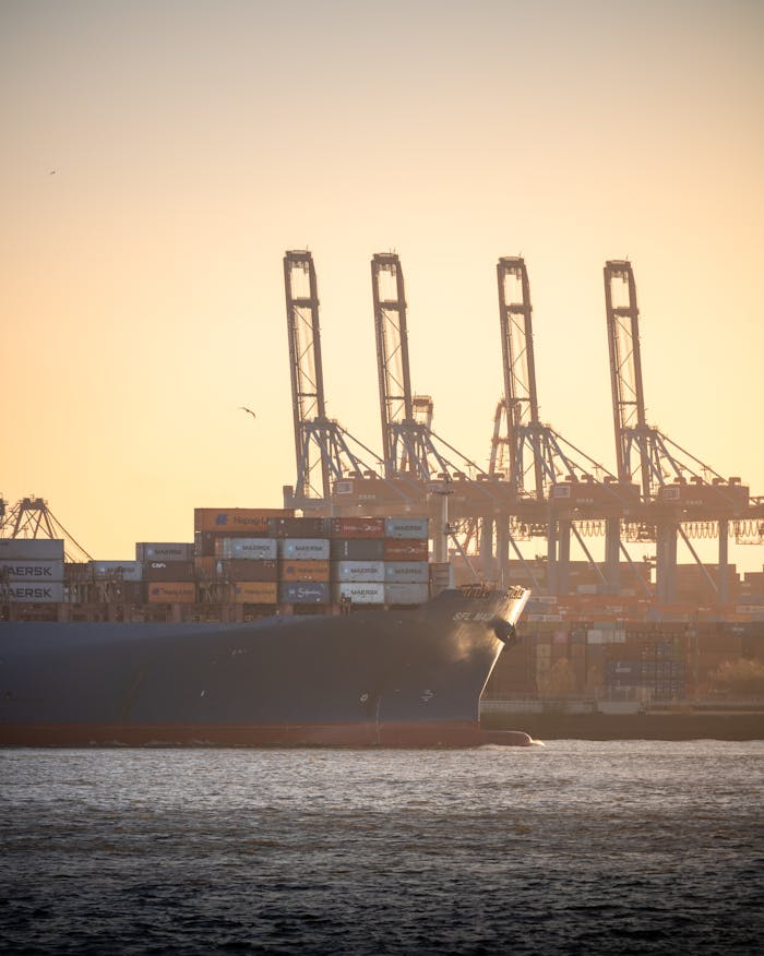 creative-03 Container ship navigating Hamburg Harbor with cranes at sunset, showcasing global trade.